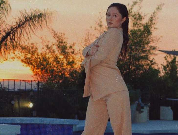 Picture of Emma Rose Kenny posing for photo in fancy casual wear with beautiful orange colored sky, tree and swimming pool in background.